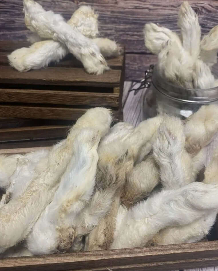 A rustic display of dried furry rabbit feet, arranged in wooden crates and a glass jar on a wooden surface.