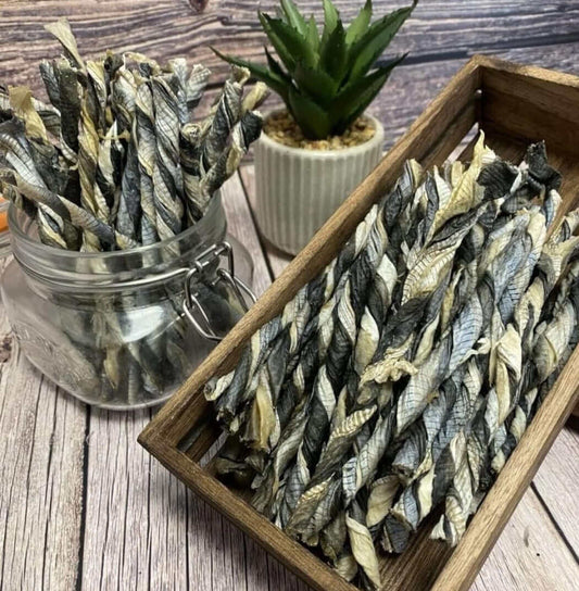 Fish skin dog chews in glass jar and wooden tray with a potted succulent plant in the background on a wooden table.