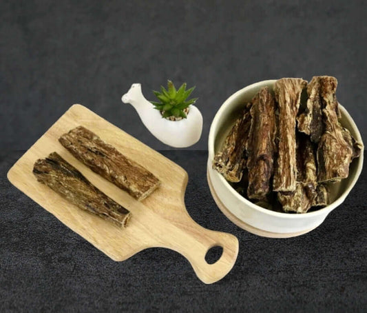 Wooden board and bowl with dried meat slices next to a white plant holder and succulent on a dark background